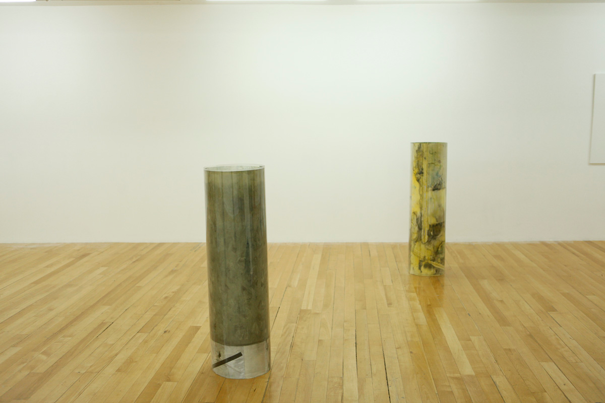 Sculpture installation where a series of drawings are rolled up between two polycarbonate sheets, creating a tube like shape standing vertically and aligned in a line, detail of two of them