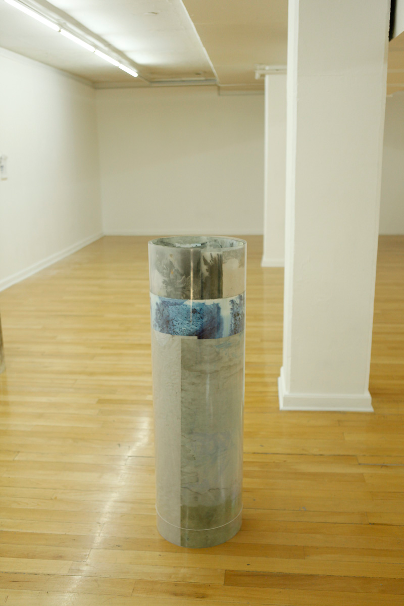 Sculpture installation where a series of drawings are rolled up between two polycarbonate sheets, creating a tube like shape standing vertically and aligned in a line, detail of only one of them