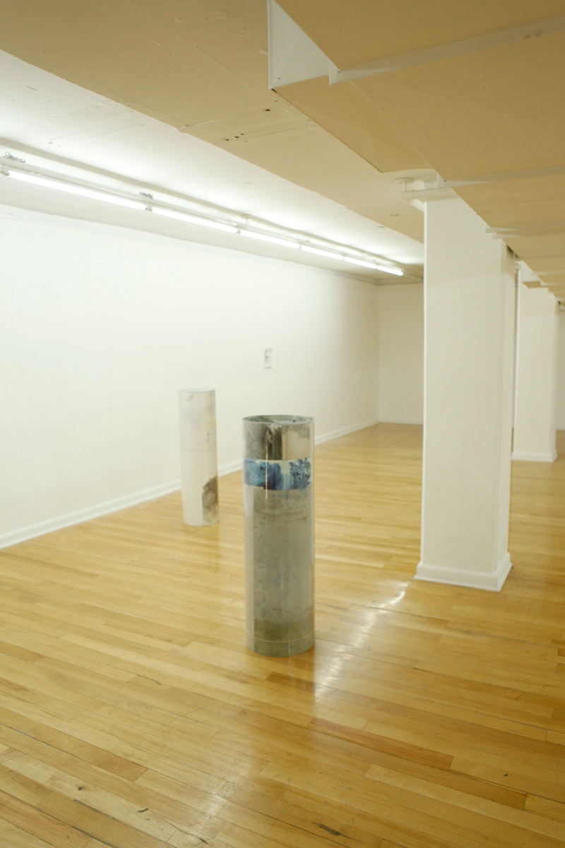 Sculpture installation where a series of drawings are rolled up between two polycarbonate sheets, creating a tube like shape standing vertically and aligned in a line, detail of two of them