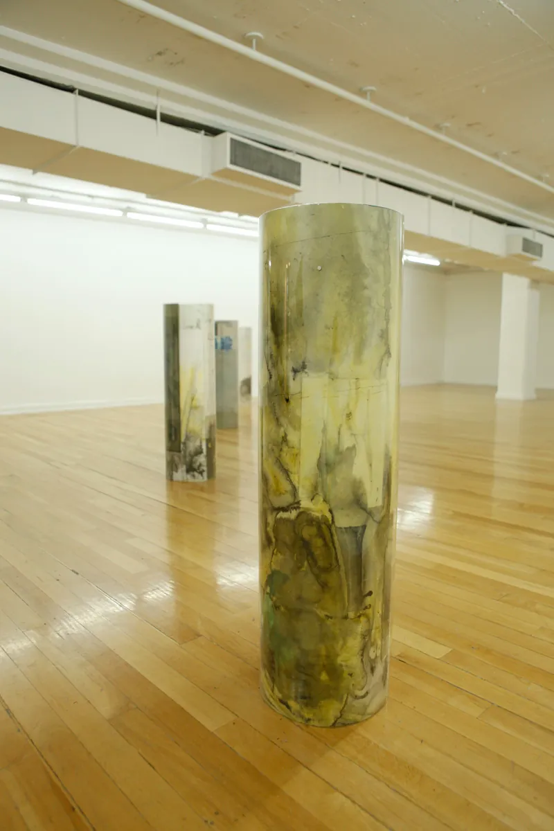 Sculpture installation where a series of drawings are rolled up between two polycarbonate sheets, seen from a point of view close to the floor, from one of the end of the line of the four tube-like sculptures