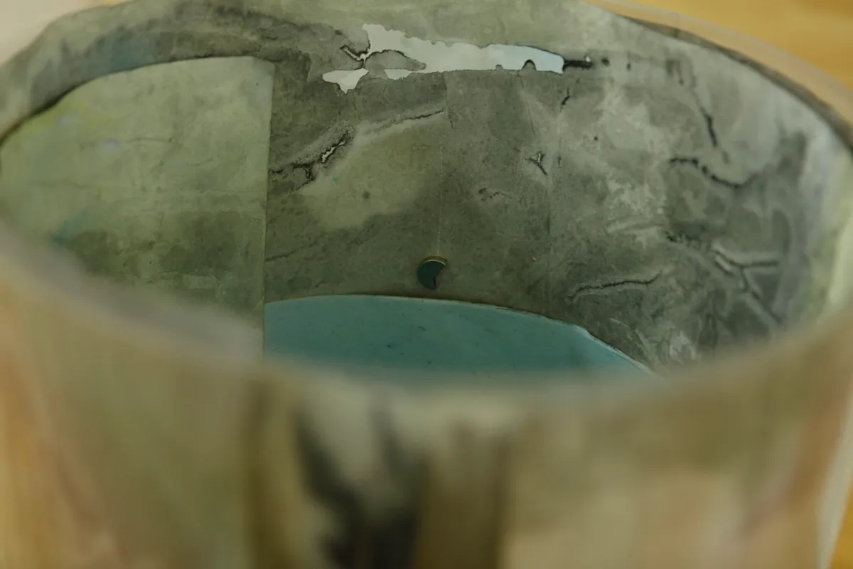 Detail of how the tube like sculpture containing drawings is looking from inside, a magnet and various layers of watercolor drawings are visible