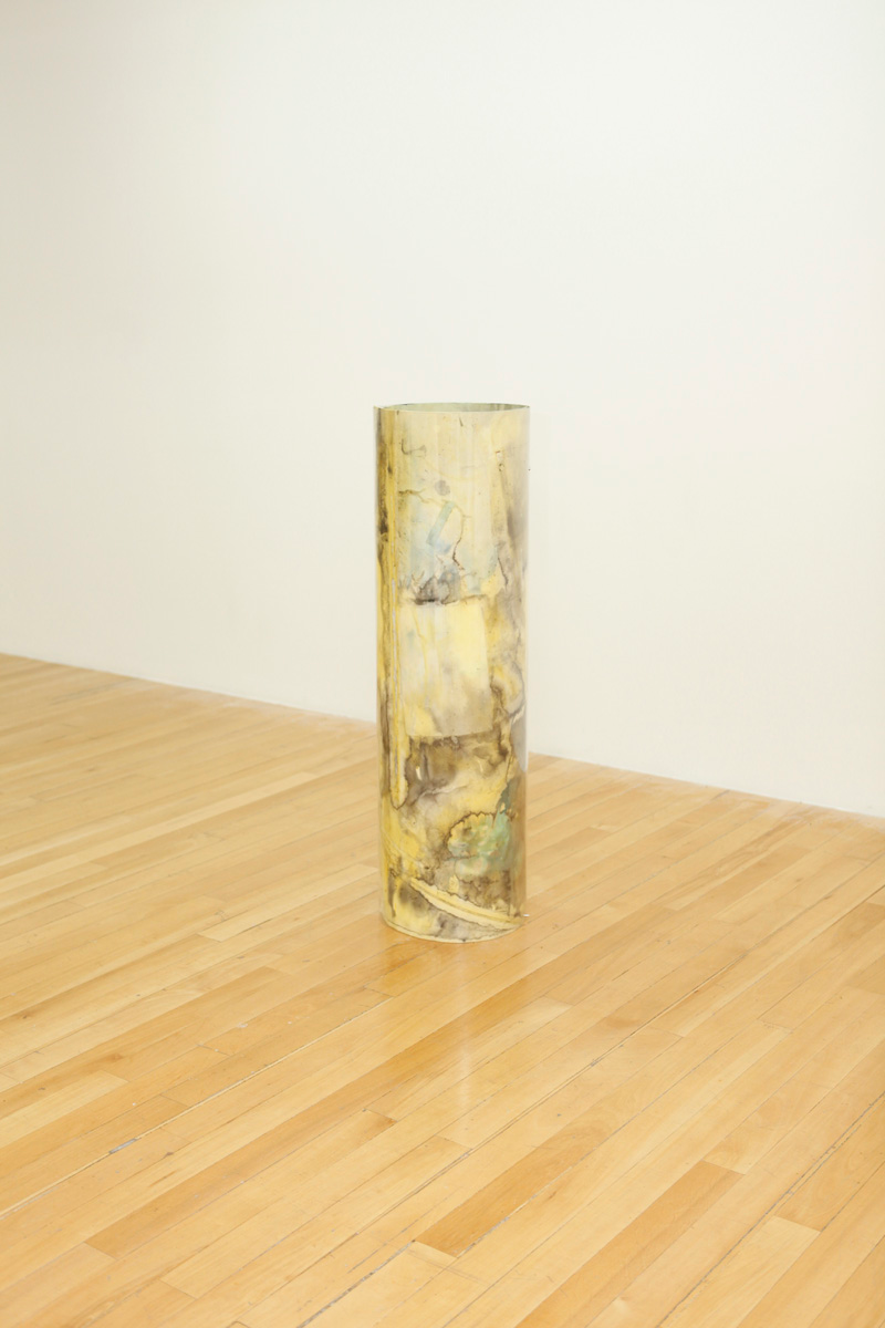 Sculpture installation where a series of drawings are rolled up between two polycarbonate sheets, creating a tube like shape standing vertically and aligned in a line, detail of only one of them