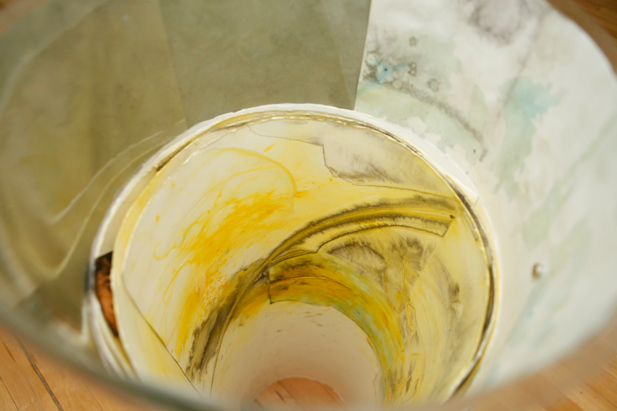 Detail of how the tube like sculpture containing drawings is looking from inside, various layers of watercolor drawings are visible and a small calendar with a puppy picture is hanging there, in between the drawings