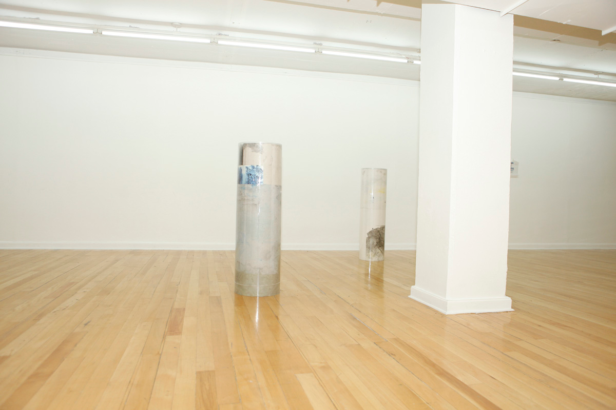 Sculpture installation where a series of drawings are rolled up between two polycarbonate sheets, creating a tube like shape standing vertically and aligned in a line, detail of two of them, the photo has a touch a touch of flashlight look