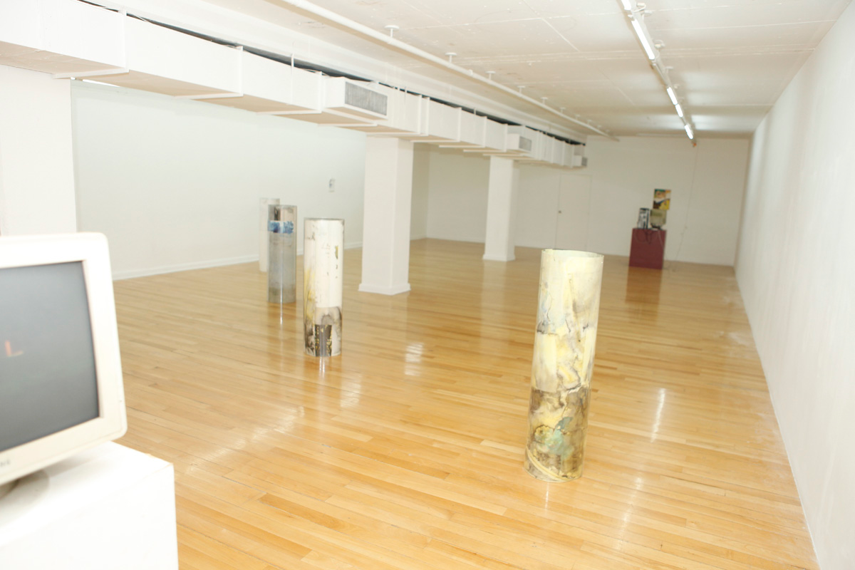 Sculpture installation where a series of drawings are rolled up between two polycarbonate sheets, creating a tube like shape standing vertically and aligned in a line, seen a bit far away from on the extreme points of the line, the picture has a touch of flashlight